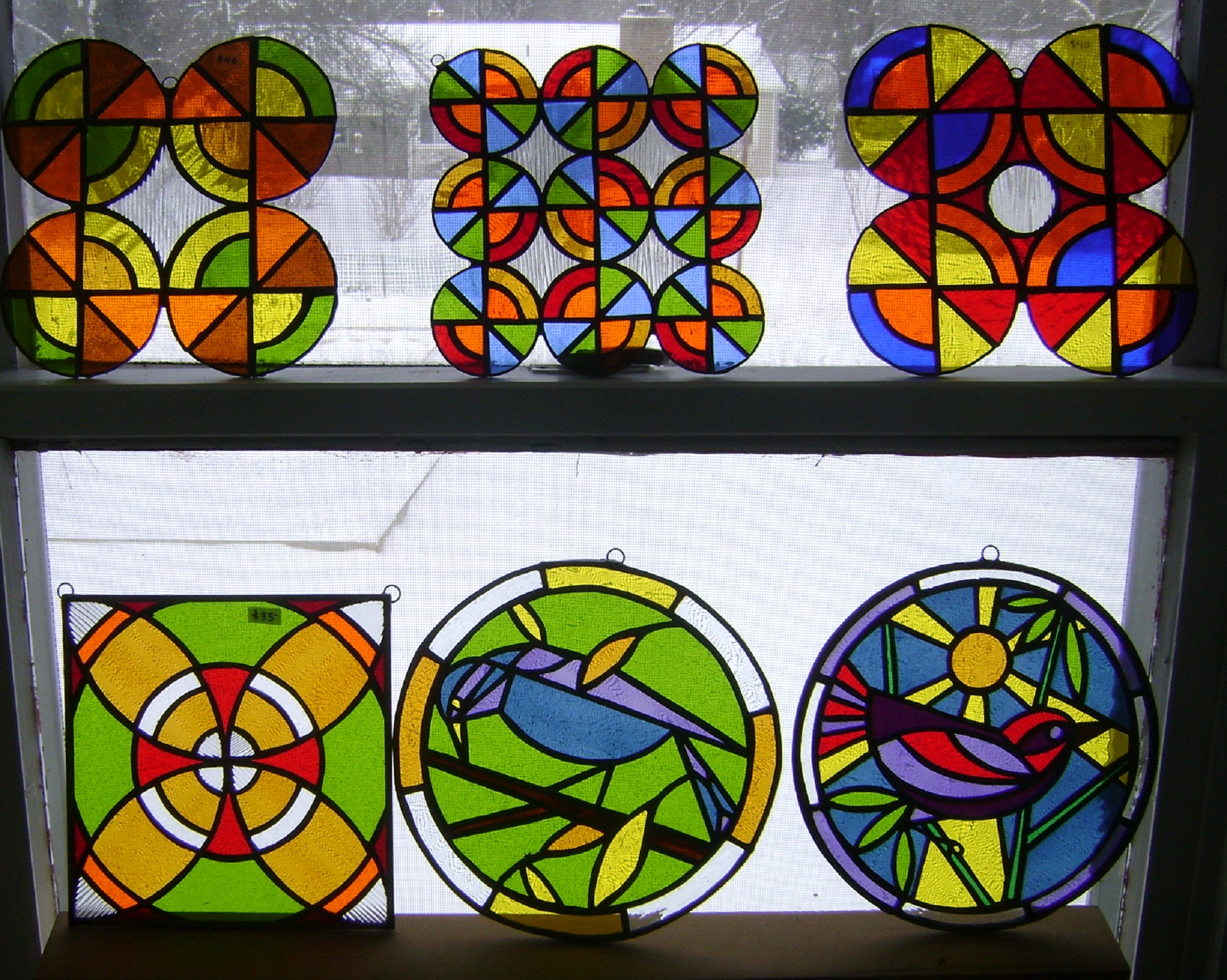 Glass art designs that feature reds, oranges and yellows with designs that are circular or birds and can hang from windows